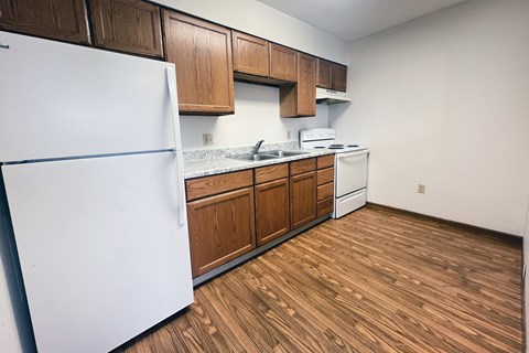 A kitchen with a white fridge, wooden cabinets, and a white stove top oven.