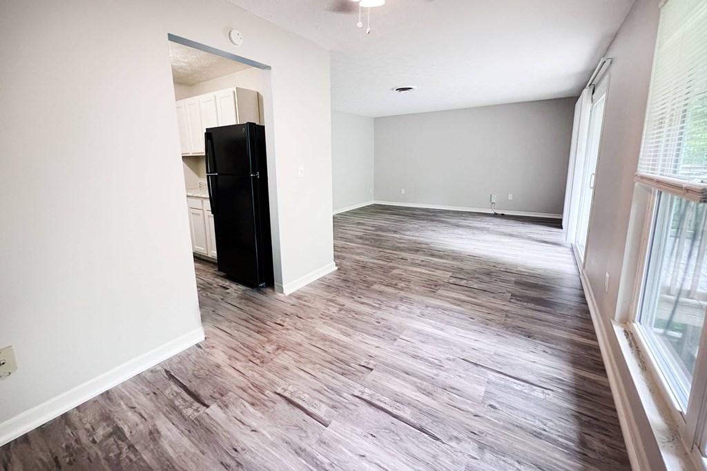 A black fridge sits in a room with wooden floors and white walls.