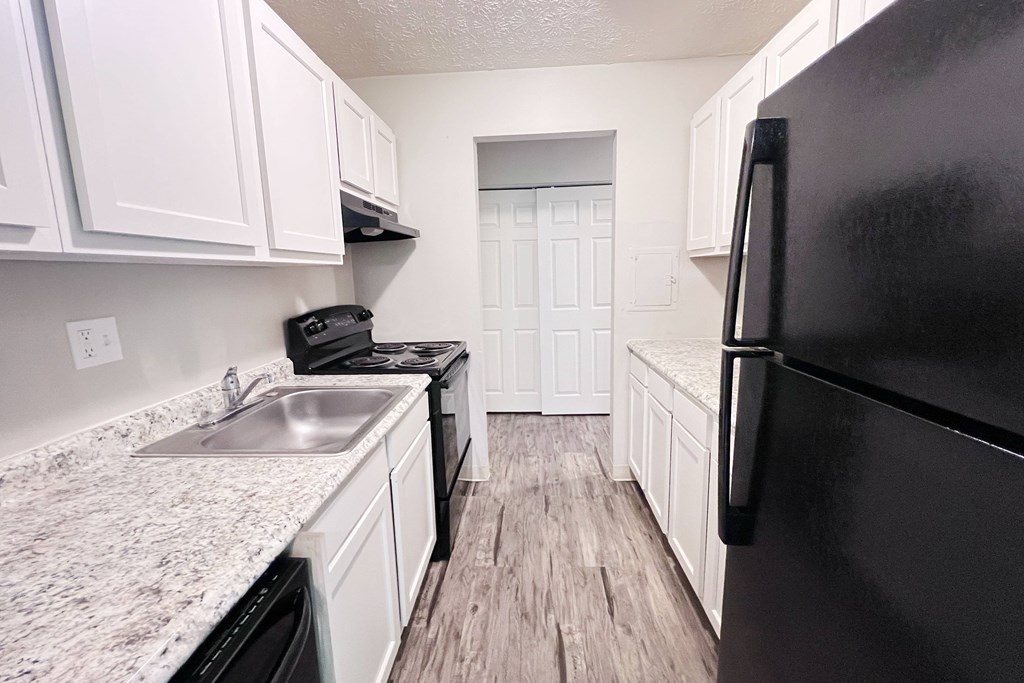 A black refrigerator sits in a kitchen with white cabinets and a marble countertop.