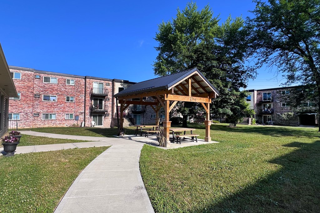 A gazebo is situated in a grassy area in front of a brick building.