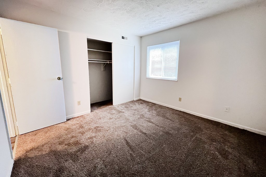 A room with a carpeted floor and a window with blinds.