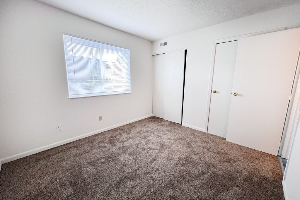 A room with a carpeted floor and a window with blinds.