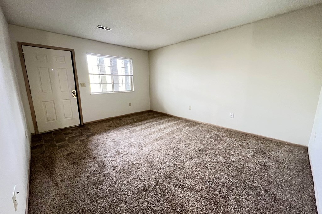an empty living room with carpet and a door at Eagle Crest Apartments, Ohio