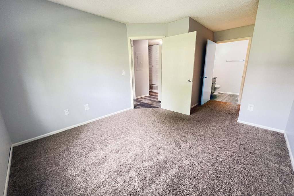 an empty living room with carpeting and a door to a bathroom at Eagle Crest Apartments, Galloway, 43119