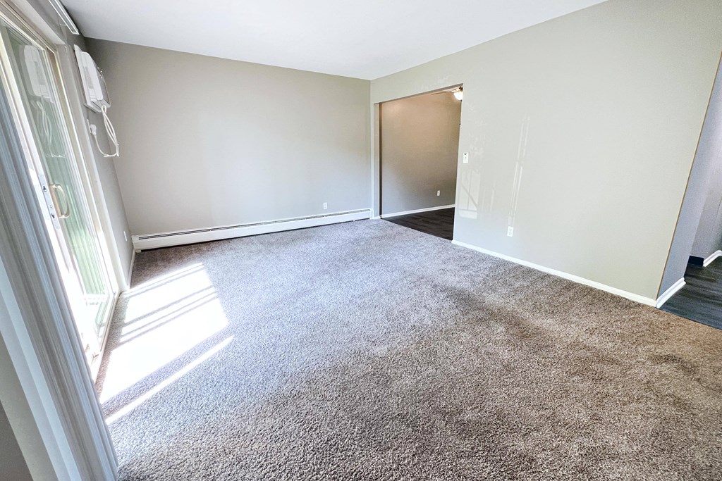an empty living room with carpet and a door to a bedroom