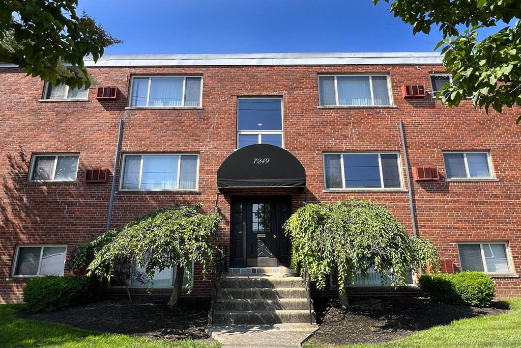 a brick building with a black awning and two trees in front