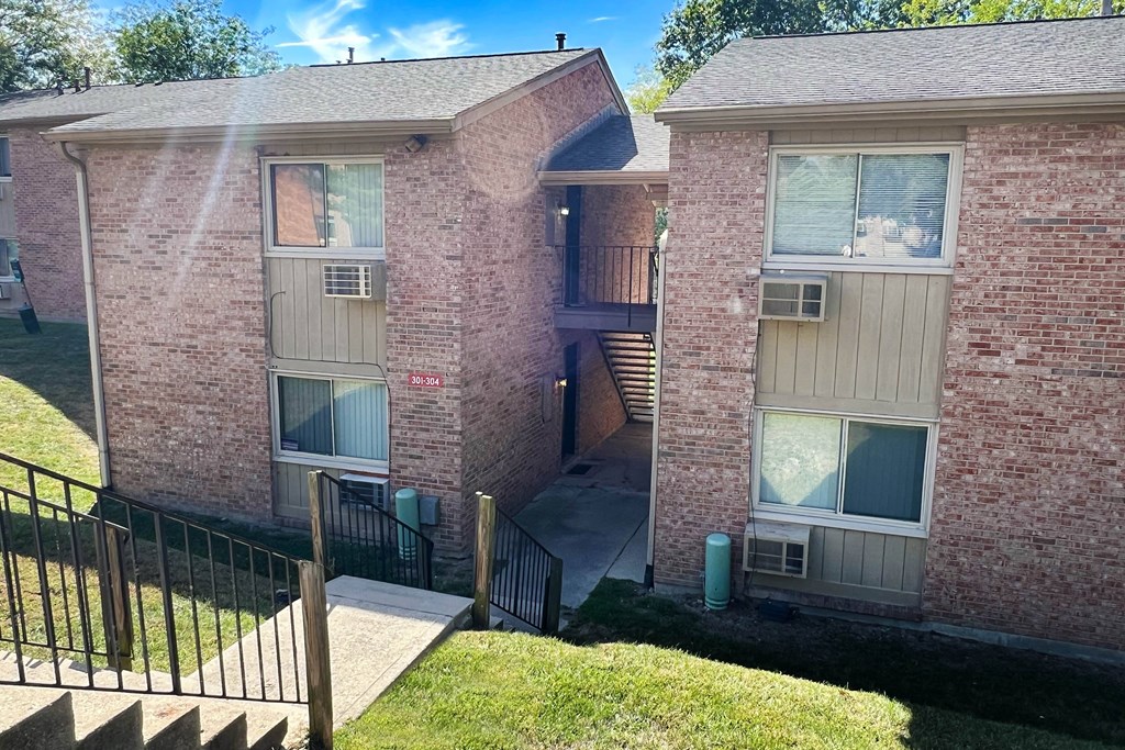 A brick apartment building with a black railing and a green trash can.