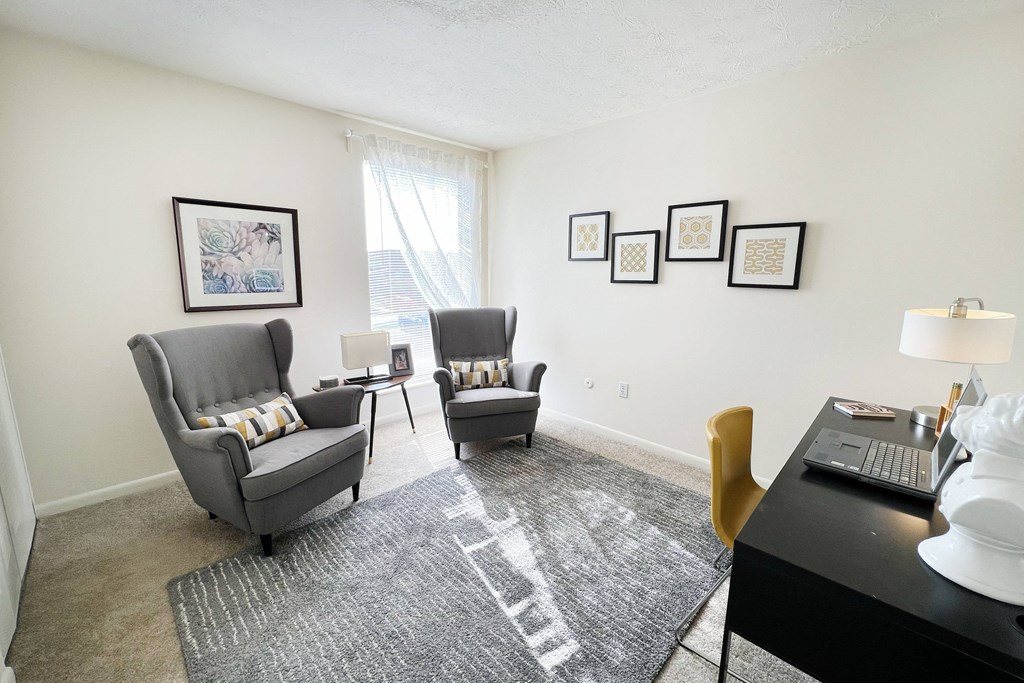 a living room with two chairs and a desk with a laptop