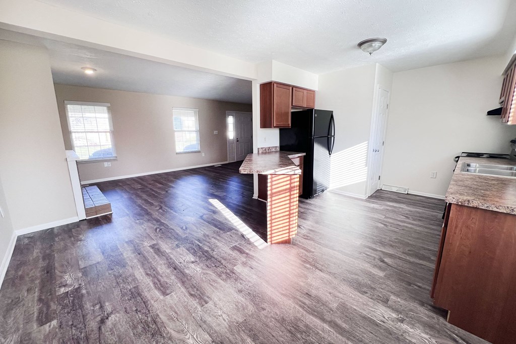 A kitchen area with a black fridge and wooden cabinets.