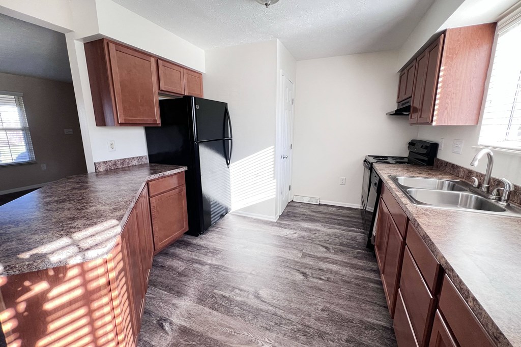 A kitchen with brown cabinets and a black refrigerator.