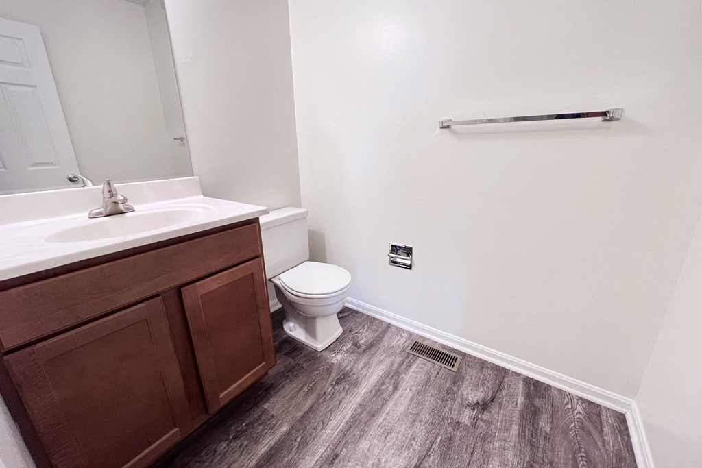 A bathroom with a toilet, sink, and wooden flooring.