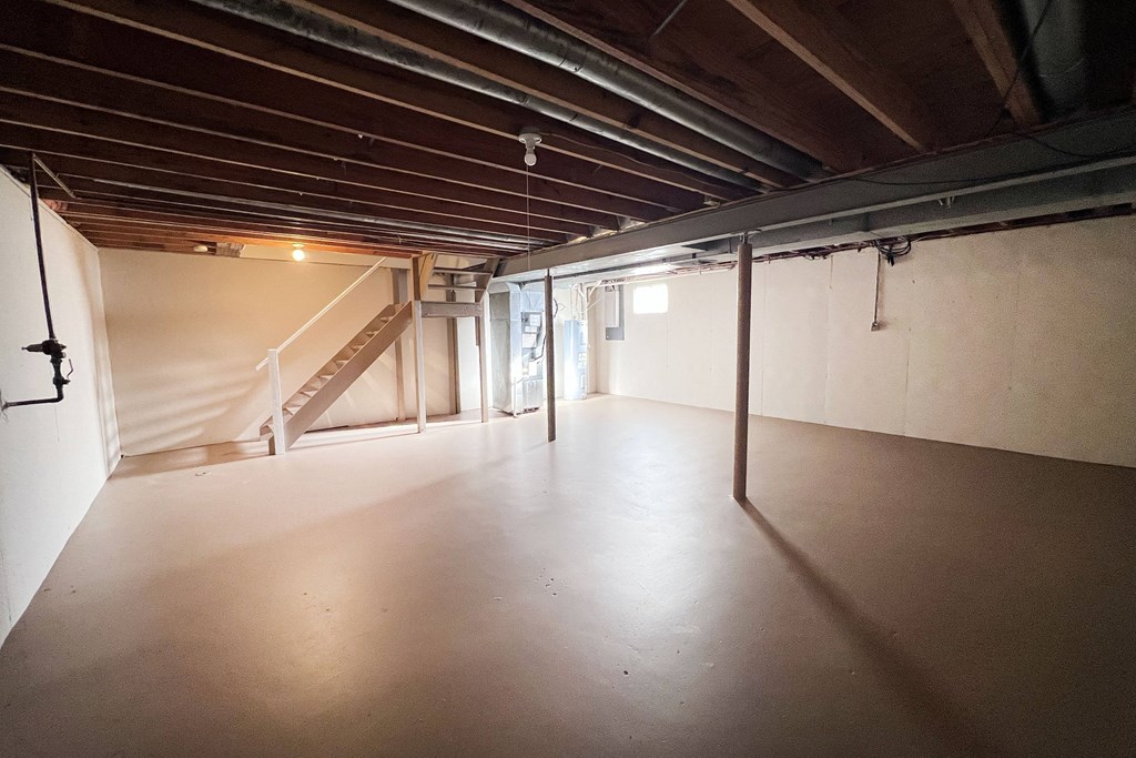 A spacious attic room with wooden beams and a staircase.