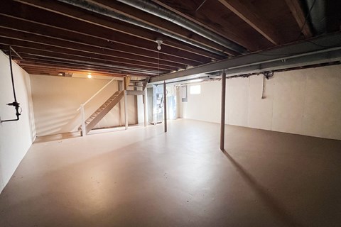 A spacious attic room with wooden beams and a staircase.