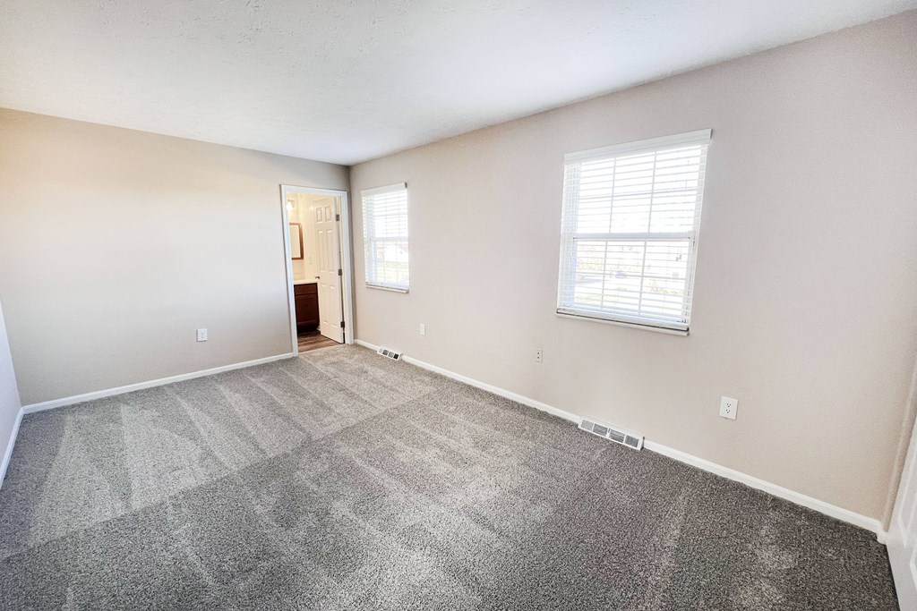 A room with a carpeted floor and a window with blinds.