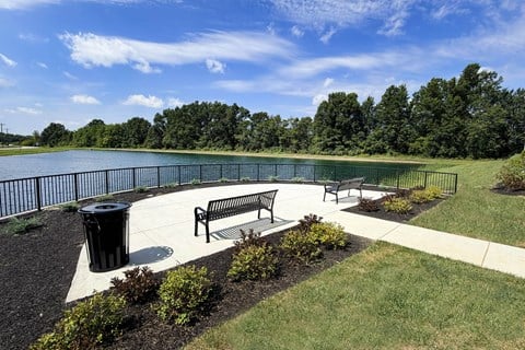A park with a bench and a trash can near a lake.