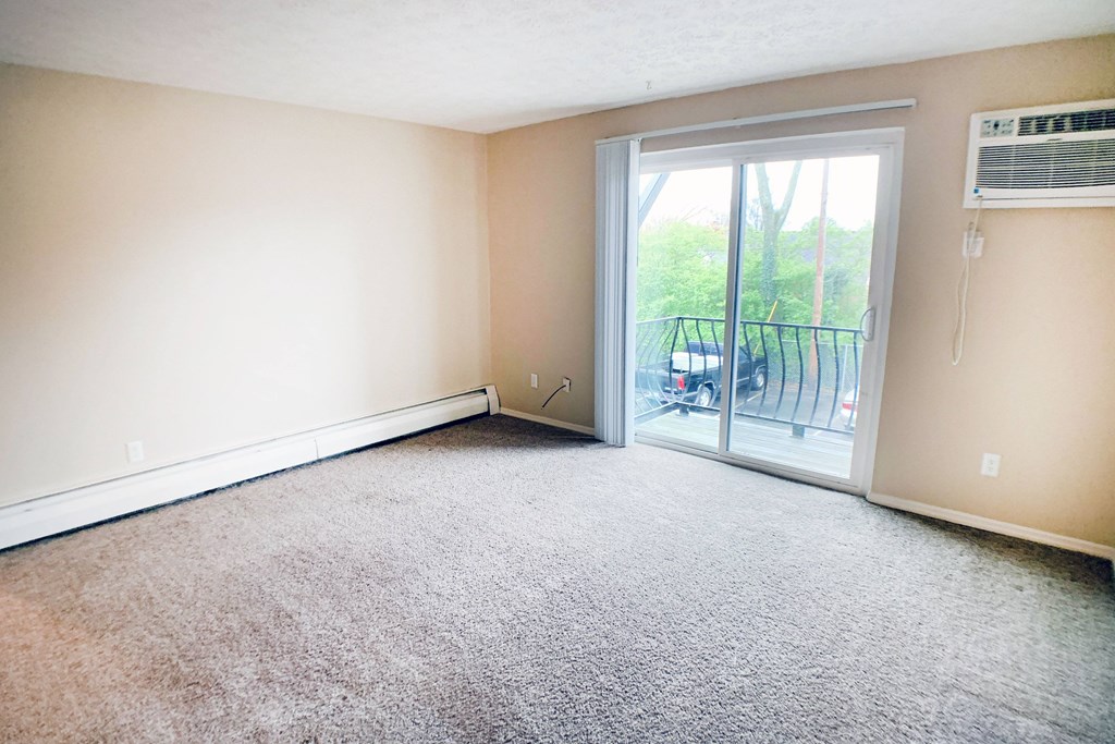 A room with a carpeted floor and a sliding glass door leading to a balcony.