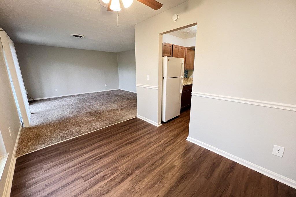 A room with a brown floor and a white fridge.