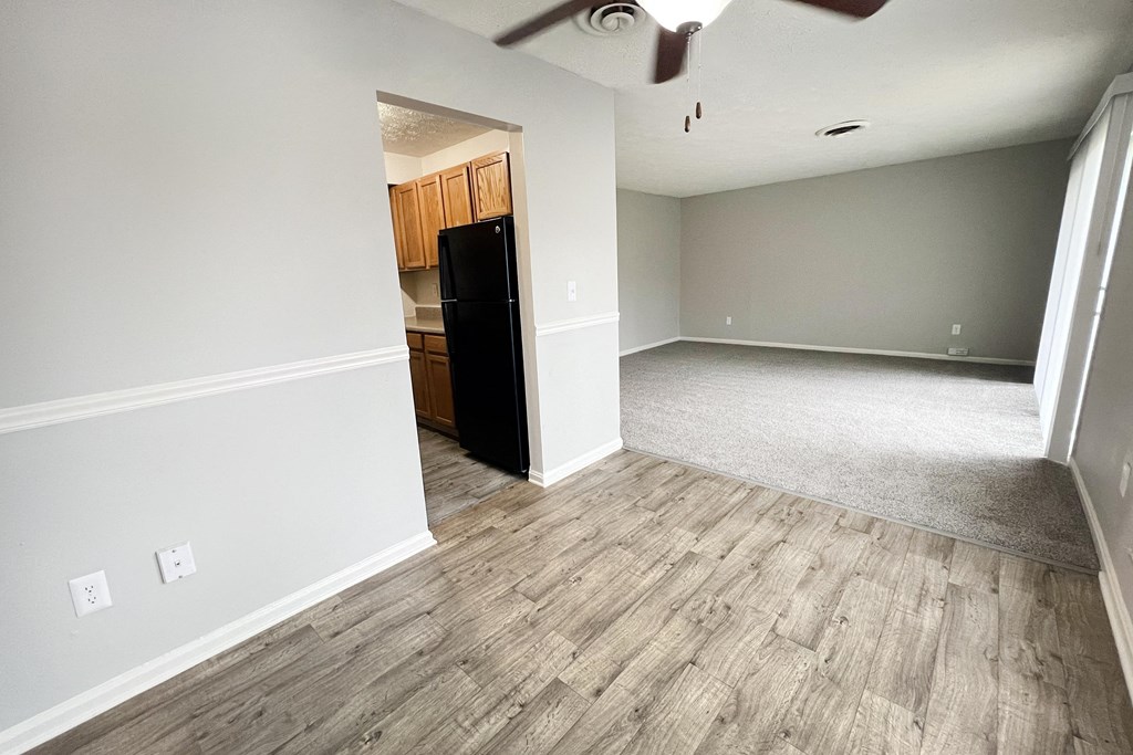 A room with a black fridge and wooden flooring.