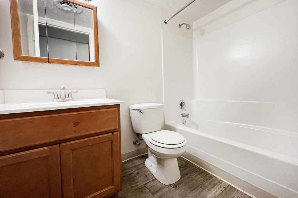 A white toilet sits in a bathroom next to a sink and a bathtub.