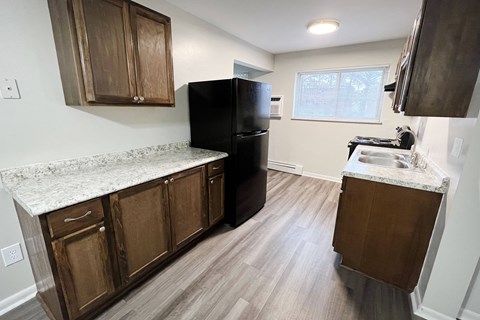 an empty kitchen with wooden cabinets and a black refrigerator  at Crown Court Apartments, Florence, KY