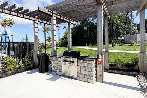 A wooden pergola with a grill and trash cans underneath it.