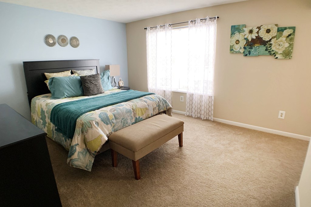 a bedroom with a bed and a chair and a window at The Vinings Apartments, Cincinnati