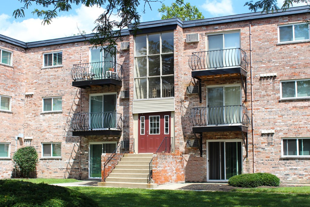 A red door is on the second floor of a brick building.