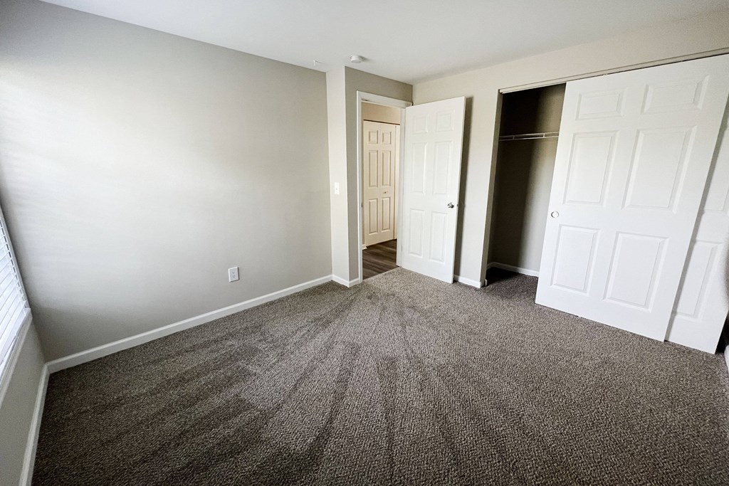 a bedroom with gray carpet and a closet with a white door  at Woodhills Apartments, West Carrollton, 45449