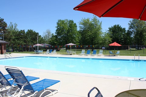 A pool with blue chairs and a red umbrella.