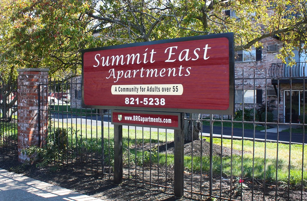 A sign for Summit East Apartments is displayed in front of a fence.