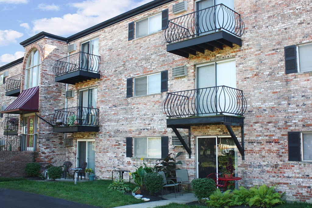 A red building with balconies and plants in front.