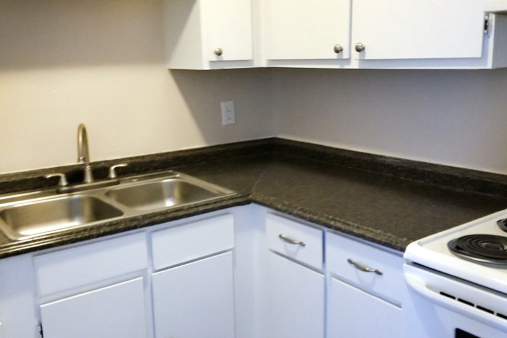 A kitchen with white cabinets and a black countertop.