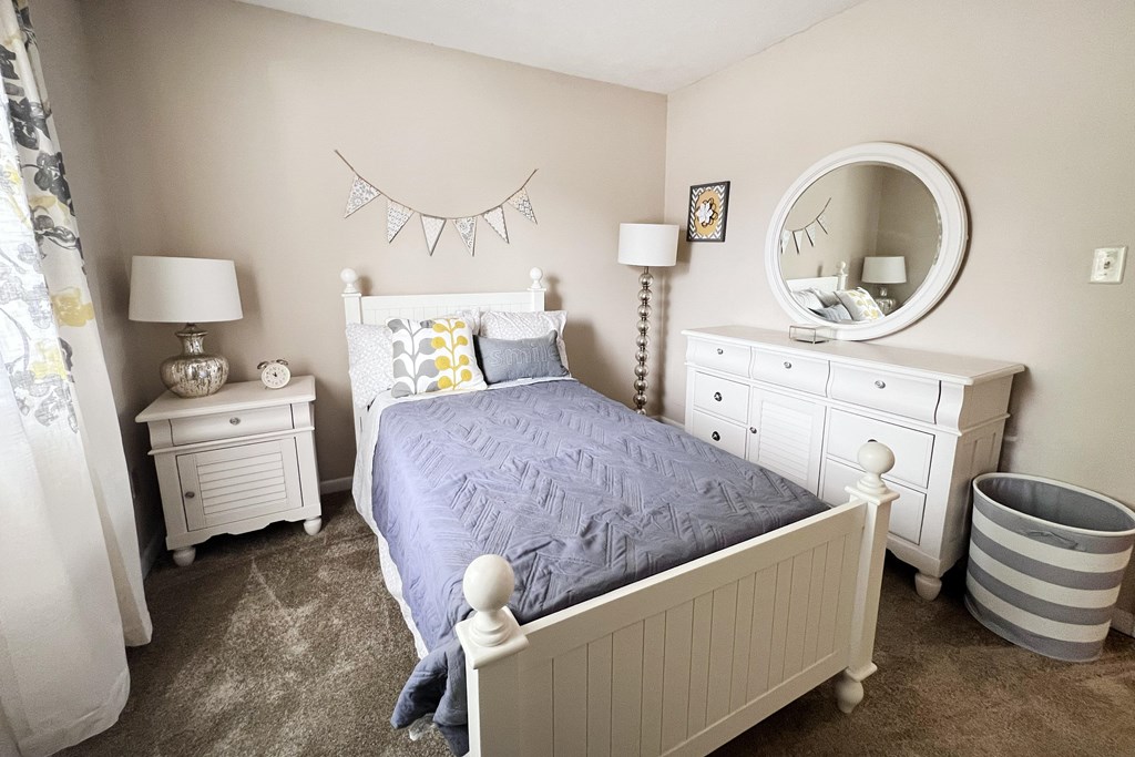 A bedroom with a white bed, dresser, and nightstand.