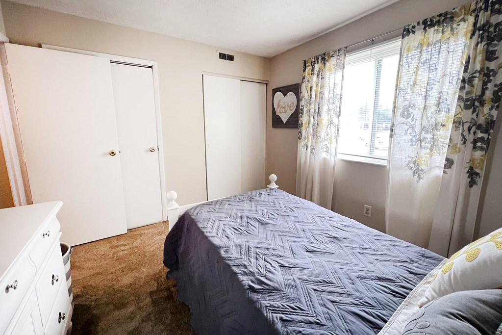 A bedroom with a bed, dresser, and window.