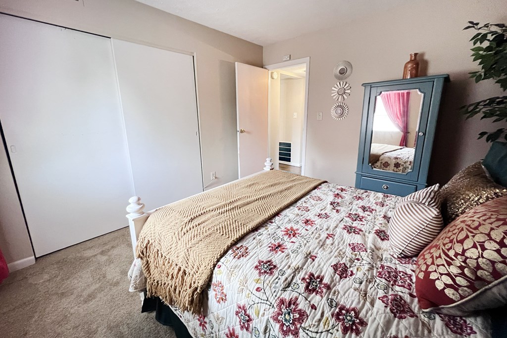 A bedroom with a bed, a mirror, and a dresser.