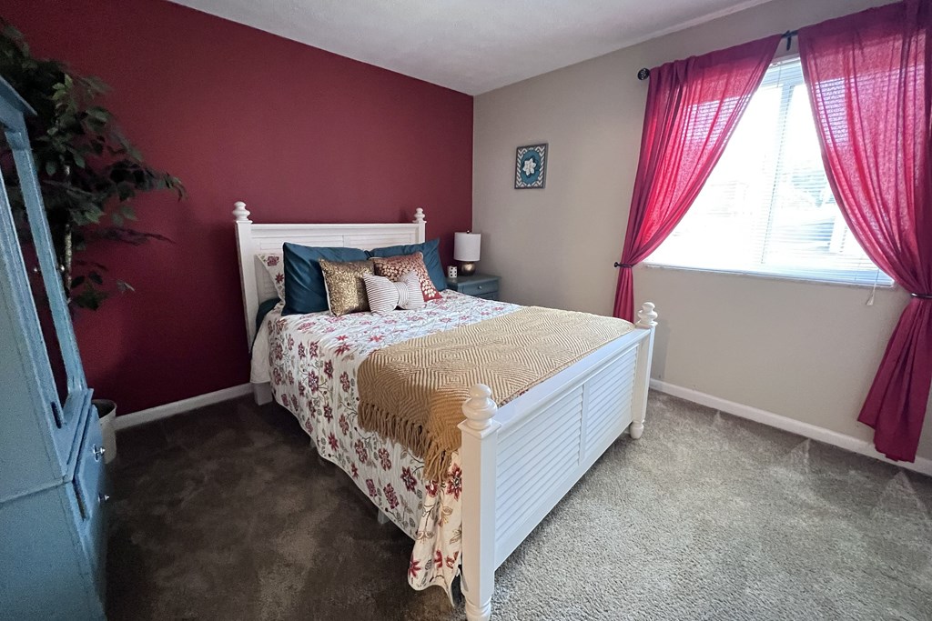A bedroom with a white bed and a red curtain.