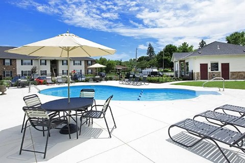 A poolside table with chairs and an umbrella is in front of a pool.