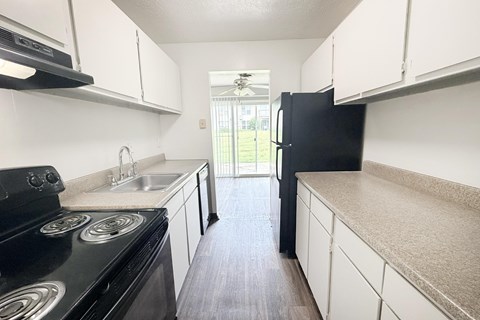 A black stove top oven sits in a kitchen with white cabinets and a black refrigerator.