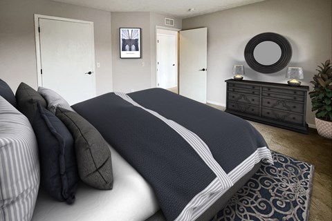 A bed with a white and navy comforter is in the foreground of a bedroom with a dresser and mirror.