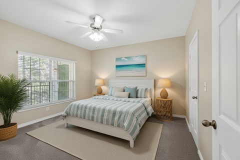 A bedroom with a bed, a ceiling fan, and a painting of a beach scene on the wall.