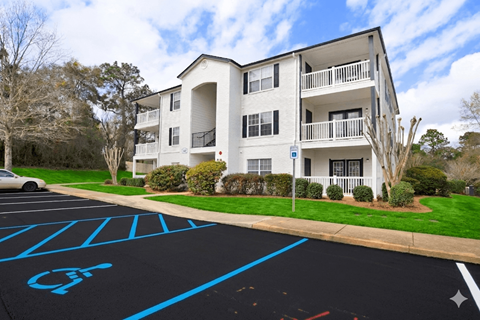 A parking lot with a handicap parking space in front of a white apartment building.
