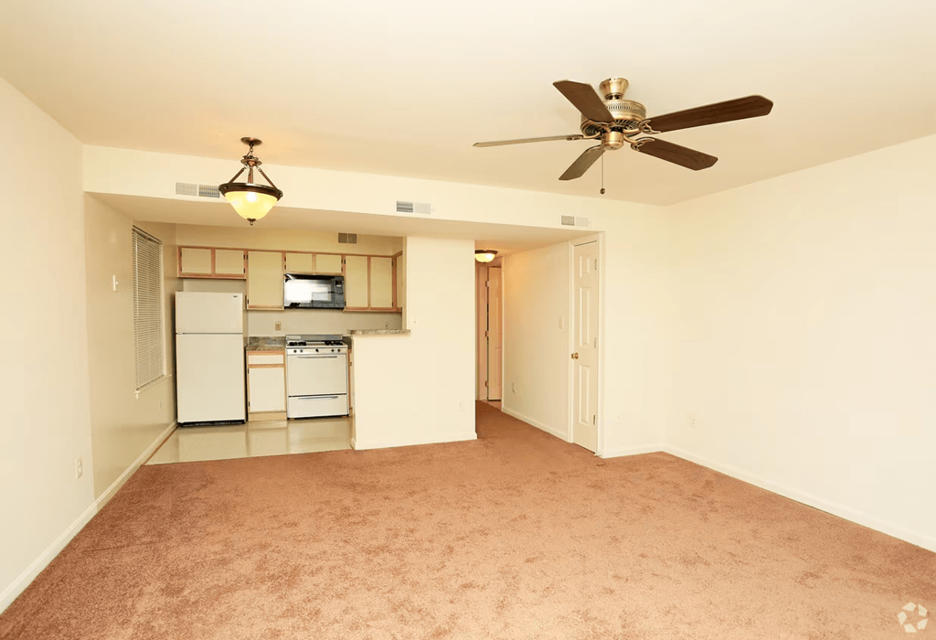 a empty living room with a ceiling fan and a kitchen