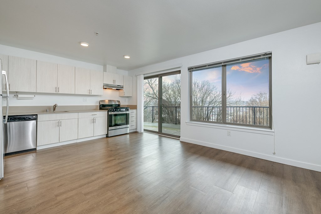 an empty living room with a large window and a kitchen
