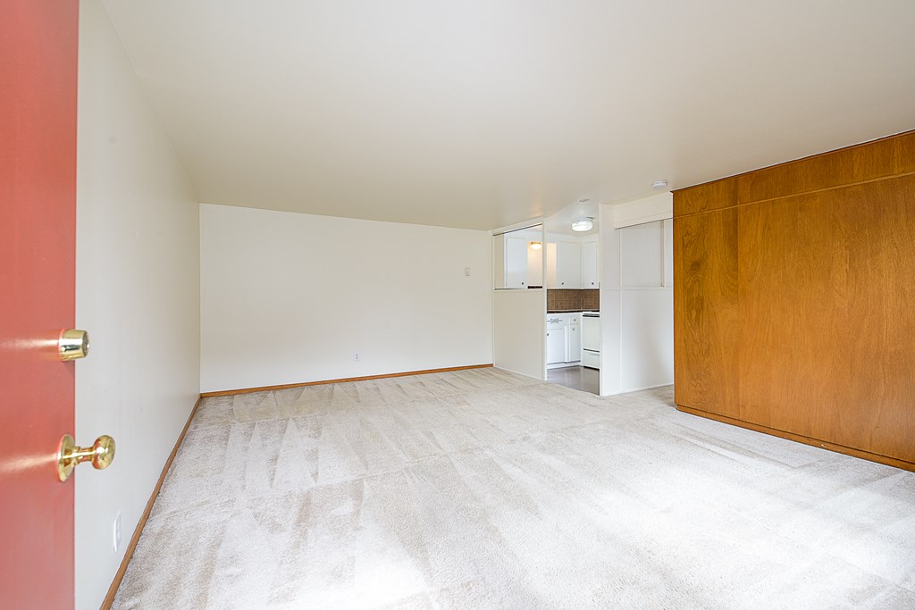 an empty living room with a wooden door and a kitchen