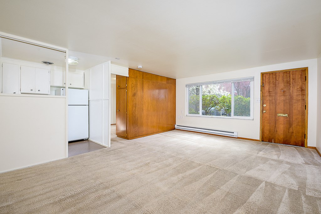 an empty living room with a kitchen and a window