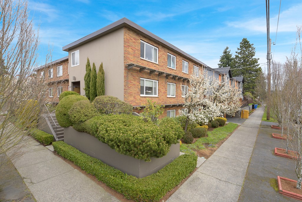 the front of a building with a sidewalk and hedges