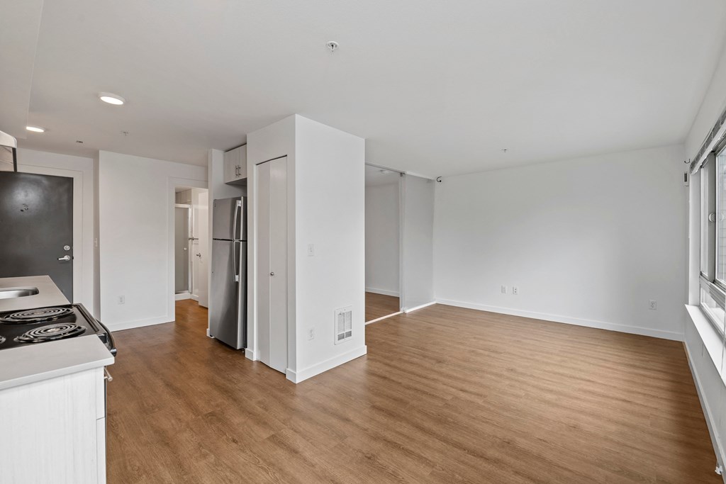 an empty living room and kitchen with white walls and wood flooring