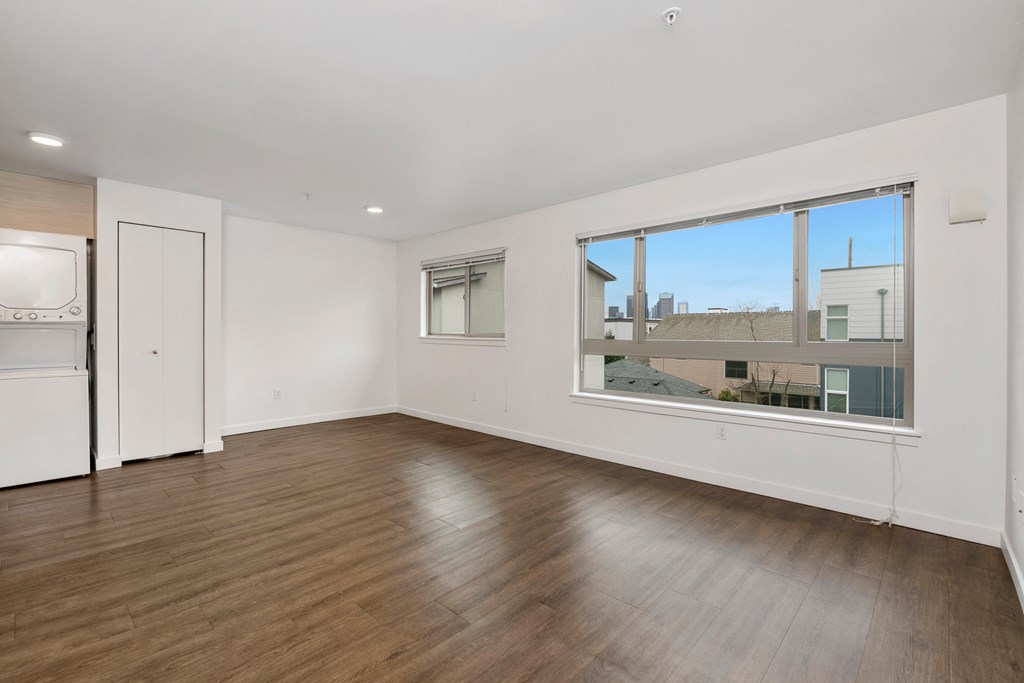 an empty living room with a large window and a kitchen