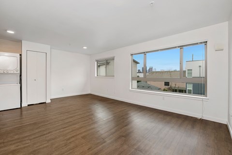 an empty living room with a large window and a kitchen