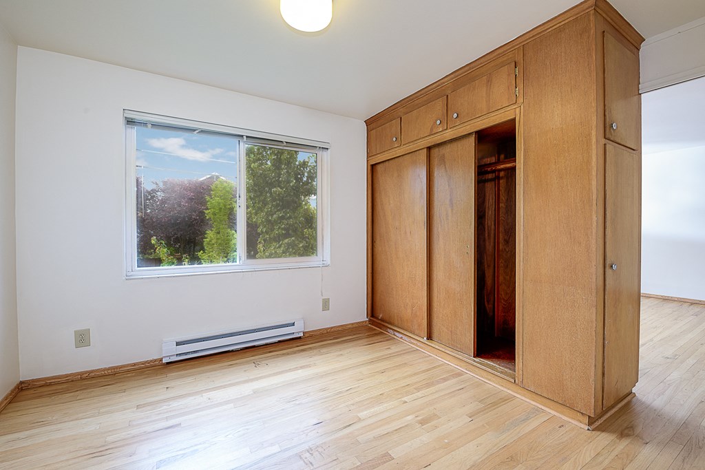 an empty room with wooden flooring and wooden cabinets and a window